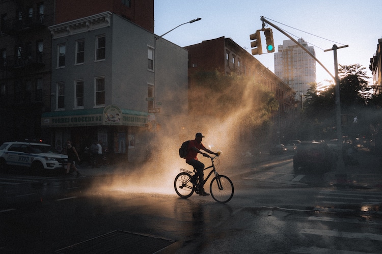 Man Riding Bike in Brooklyn in Front of Open Fire Hydrant